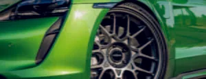 Rotiform-bild-1 Närbild av framhjulet på en sportbil med klargrön metallic-lack. Fälgen är mörkgrå med många ekrar och har Rotiform-logotypen i centrum, monterad med lågprofil Michelin-däck. Den blanka karossen och strålkastaren syns i kanten, och den intensiva gröna färgen reflekterar ljuset tydligt, vilket ger ett exklusivt och sportigt intryck.